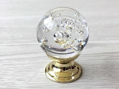 a clear glass ball on a gold plated stand with white woodgrain background