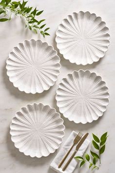 four white plates with leaves on them and gold cutlery next to each other in front of a marble background