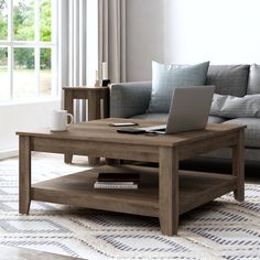 a coffee table with a laptop on it in front of a couch and large windows