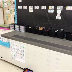 a classroom desk with lots of black buckets and writing on the wall behind it