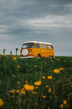 an orange and white van is parked in the middle of a field with yellow flowers