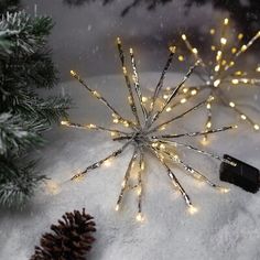 a christmas tree with lights on it in the snow next to a small pine cone