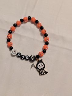 A hand-crafted Halloween themed beaded bracelet with orange, black, and white beads and a cute reaper charm. Halloween Diy Bracelets, Novelty Black Beaded Bracelets For Halloween, Novelty Orange Bracelets For Halloween, Halloween Novelty Orange Bracelets, Black Beaded Bracelet For Halloween, Black Beaded Stretch Bracelet For Halloween, Orange Beaded Bracelets For Halloween Gift, Handmade Orange Bracelets For Halloween, Orange Halloween Gift Bracelet