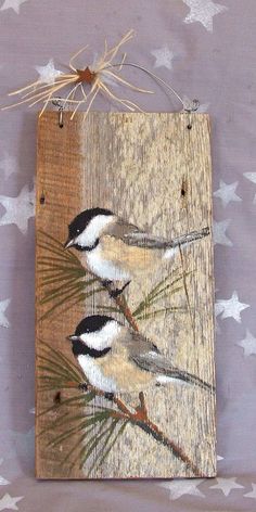 two birds sitting on top of a piece of wood with pine needles hanging from it