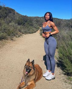 a woman standing next to a dog on a dirt road