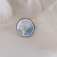 a blue and white brooch sitting on top of a feathery object with some feathers in the background