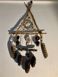 a clock with feathers hanging from it's side on a white wall next to pine cones