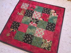 a red and black quilted table topper on the floor next to a white rug