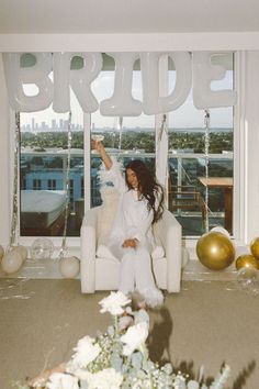 a woman sitting on a white chair in front of balloons that spell out the word bride