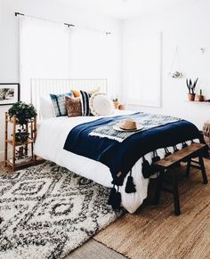 a bedroom with a bed, rug and window in the corner that has plants on it