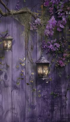 two lanterns are on the side of a wooden fence with purple flowers growing over it