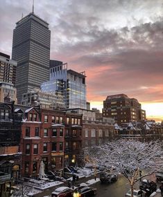 the city skyline is covered in snow as the sun sets over buildings and parked cars