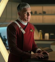 a man in a red star trek uniform standing next to a table with a laptop on it