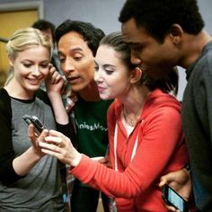 a group of young people standing around each other looking at a cell phone and smiling