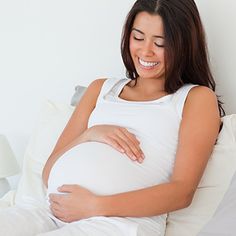 a pregnant woman laying in bed with her stomach wrapped around her belly and smiling at the camera