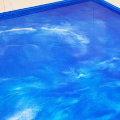 an empty swimming pool with blue water and white clouds painted on the wall behind it