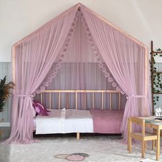 a pink canopy bed sitting in a bedroom next to a table