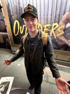 a young man standing in front of a sign with his hands out to the side