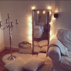 a living room with white furniture and lights on the wall above it, along with a large mirror