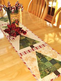 a table runner with christmas decorations on it and a vase filled with flowers in the center