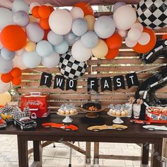 a table topped with lots of balloons and cake next to a sign that says two fast