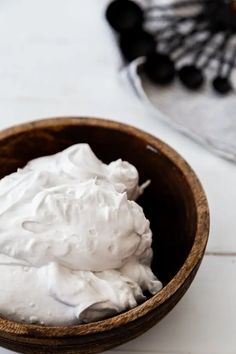 a wooden bowl filled with whipped cream on top of a white tablecloth next to an empty napkin