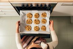 a woman placing cookies on top of an oven