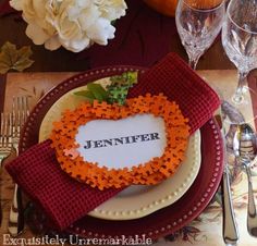 a place setting with napkins, flowers and wine glasses on the table for an autumn themed dinner