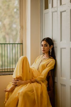 a woman sitting on a chair in front of a window wearing a bright yellow outfit