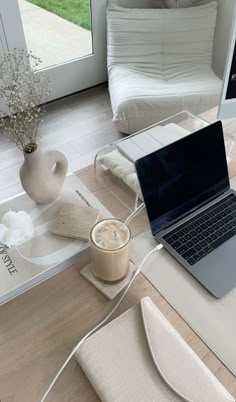 an open laptop computer sitting on top of a wooden table next to a vase with flowers