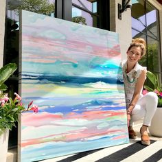 a woman standing next to a large painting on the side of a building with potted plants in front of it