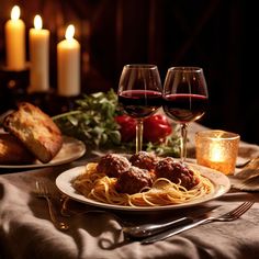 two glasses of red wine and spaghetti on a table with bread, tomatoes, meatballs and other food