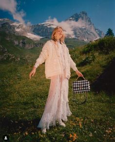 a woman standing on top of a lush green hillside holding a black and white purse