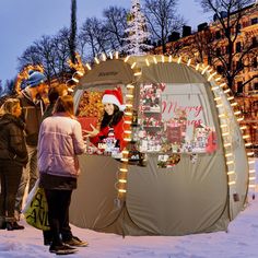 a group of people standing around a tent with christmas decorations on the front and side