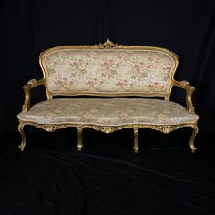 an old fashioned couch with floral fabric on it's back and arm rests against a black backdrop