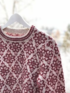 a red and white sweater hanging on a hanger in front of snow covered trees