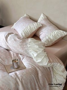 a bed with pink comforter and pillows on it, next to a cup of coffee