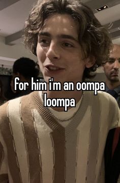 a young man with curly hair wearing a striped sweater and looking at the camera while standing in