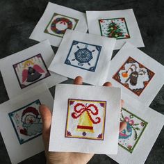 someone holding up some cross stitch cards with christmas designs on them, all in different shapes and sizes