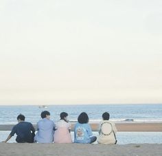 four people sitting on the beach looking out at the ocean