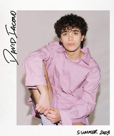 a young man with curly hair wearing a pink shirt and holding a pair of scissors