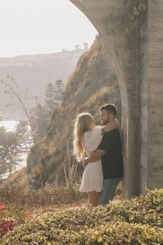 a man and woman embracing each other in front of a stone arch over looking the ocean