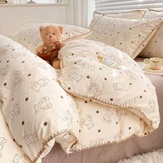 a teddy bear sitting on top of a bed in a room with white sheets and pillows