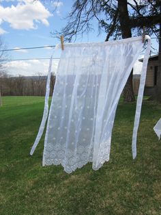 a white sheer curtain hanging from a clothes line in the grass next to a tree