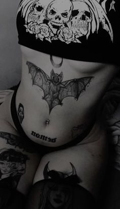 a woman with tattoos on her stomach wearing a bat and skull headdress in black and white