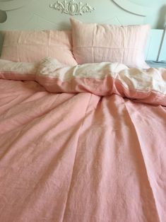 an unmade bed with pink linens and white pillows on top of the headboard