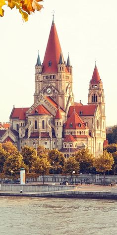 an old building with red roof and spires next to the water on a sunny day