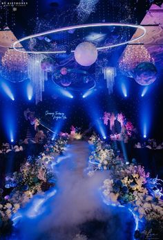 a stage set up for a show with blue lights and flowers on the floor, surrounded by balloons