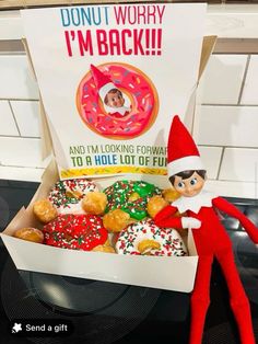 an elf is sitting next to a box of doughnuts