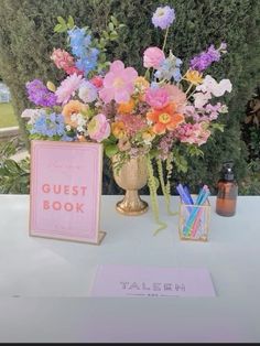 a vase filled with lots of colorful flowers next to a sign that says guest book